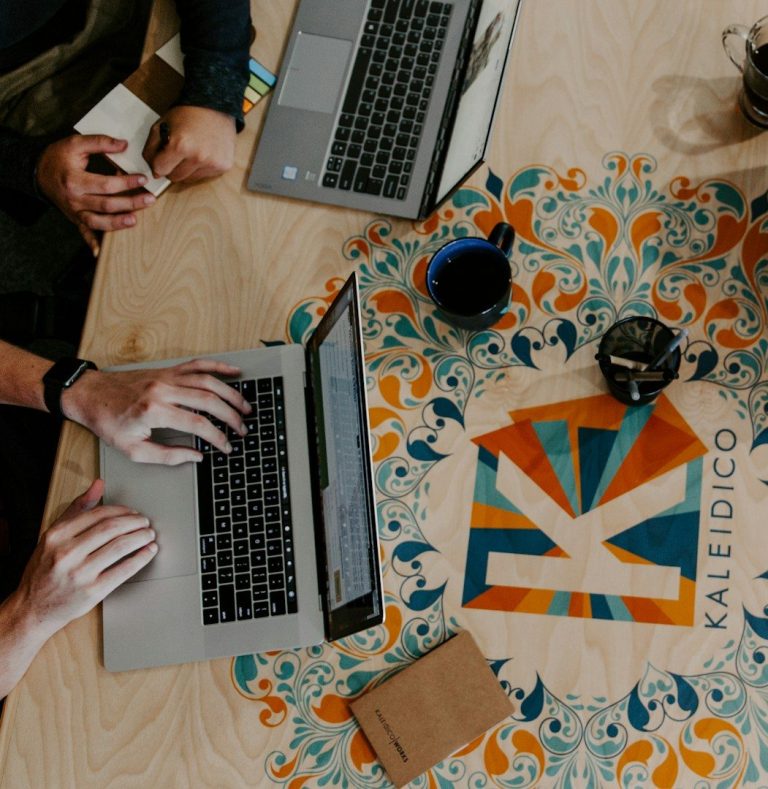 Hands typing on laptops, with a colourful table design and coffee cups.